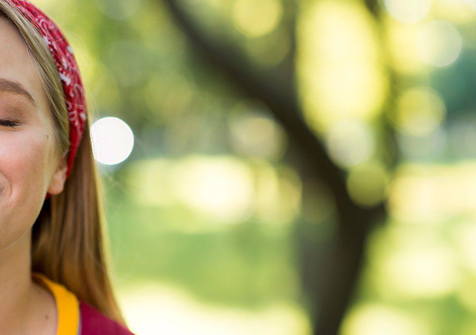 Primer plano de una chica sonriendo. Fondo difuminado de bosque o parque.