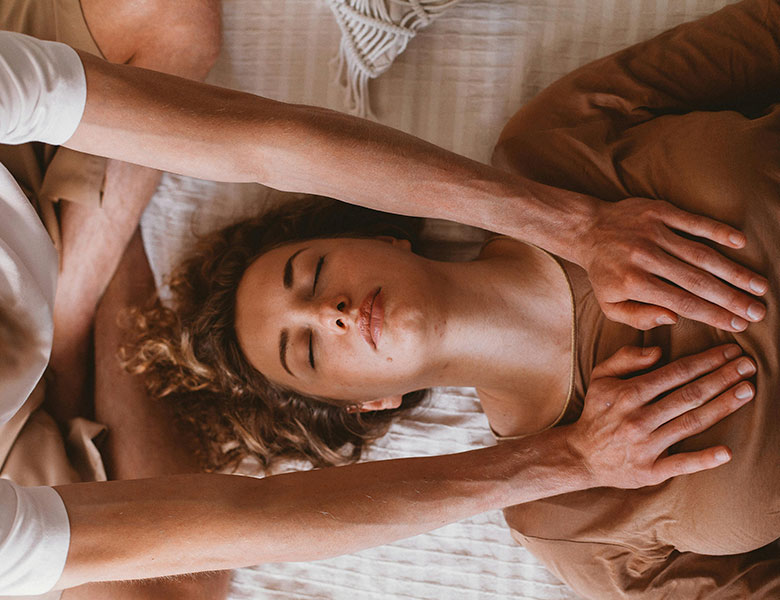 Mujer tumbada con los ojos cerrados y otra persona poniendo las manos sobre su pecho