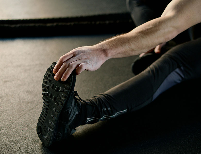 Hombre sentado en el suelo con ropa deportiva haciendo un estiramiento de la pierna izquierda